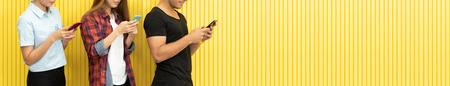 Fashion Portrait of Hipster people wear sunglasses are using smartphones and standing over the Yellow wall background. Urban Fashion Concept.の写真素材