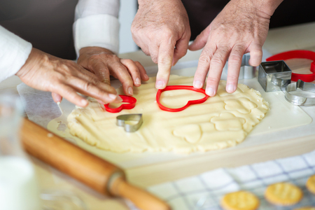 Close up Elderly Hands are making cookies with red cutters in heart shape.の写真素材