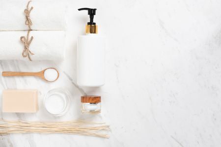 Top view of Cosmetic bottles, soap, wooden spoon and towel on white marble background. Spa products with copy space.の写真素材
