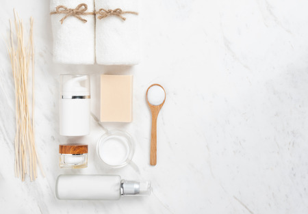 Top view of Cosmetic bottles, soap, wooden spoon and towel on white marble background. Spa products with copy space.の写真素材