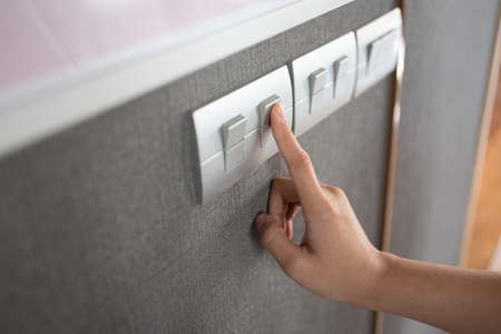 Asian female right hand is turning on or off on grey light switch over textile texture wall. Copy...
