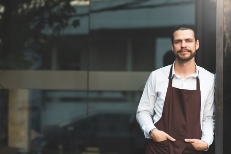 Successful SME. Male Barista Leaning against on front of the coffee shop glass wall. Portrait of...