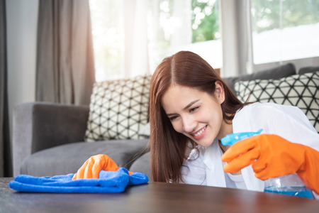 Happy Beautiful woman in white shirt is cleaning on top of table with using spray and duster....
