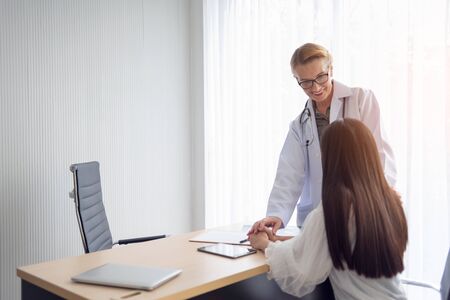 Smiling Senior Female Doctor talking and reassuring her patient in the medical office.の写真素材