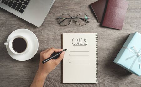 Top view of Man hand is planning and writing to do list and goals in a notebook for New year,...