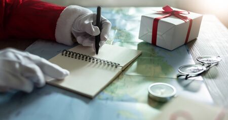 Santa claus hands is planning and writing on notebook and world map for christmas tripsの写真素材