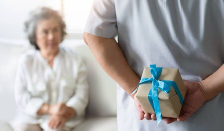 Making a surprise for Christmas and New year concept. Asian Senior man hiding gift box behind his back while his wife sitting and looking to him at their house.の写真素材