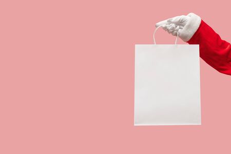 Santa Claus hand holding pink shopping bag on isolated background. Black Friday, Sales, Giving Gift for Christmas and New Year 2019 concepts.の写真素材