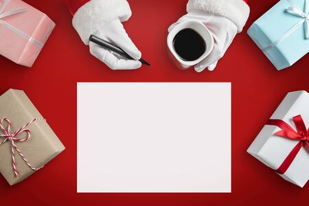 Top view of Santa Claus hands is writing goals and to do lists in a blank paper sheet for New year, Christmas. Gift boxes on red isolated background.の写真素材
