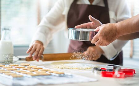 Happy Asian senior couple in brown aprons are preparing cookies in the kitchen together. Grandfather...