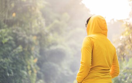 Happy woman traveler in yellow sweater with hood is standing and looking to nature on vacation concept. Rear view.の写真素材