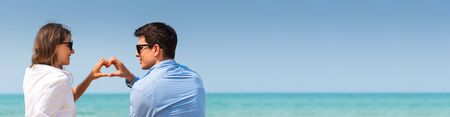 Couple In Love making heart shape with their hands over sea, sky, beach background. Valentine's day concept.の写真素材