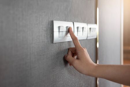 Asian female right hand is turning on or off on grey light switch over textile texture wall. Copy...