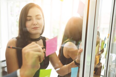 Young Businesswoman is writing the new ideas in sticky notes on glass wall.