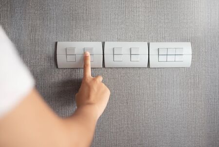 Asian female right hand is turning on or off on grey light switch over grey texture wall at the home...