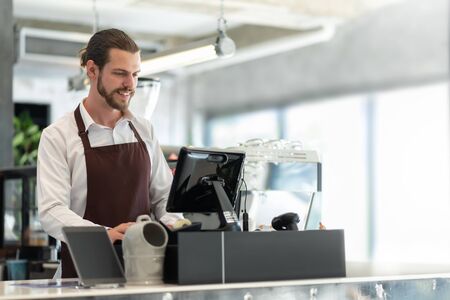 Startup of small business owner, Successful SME. Confident Male Barista working on counter at the coffee shop. Portrait of Happy smiling Bearded man wear white shirt and brown apron making coffee in cafe.の写真素材