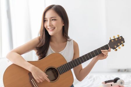 Carefree Pretty Asian woman is practicing Acoustic guitar. Happy Smiling girl enjoying with the...
