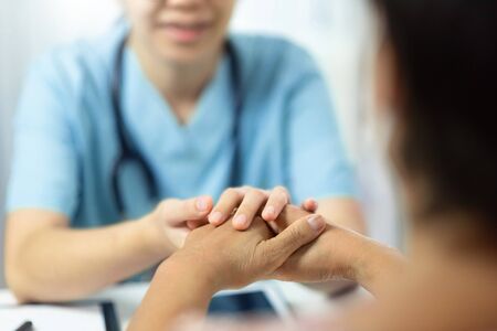 Asian medical nurse talking giving advice and comforting senior woman patient in office room. Female elderly being reassured by Physician with holding hands together in hospital.の写真素材