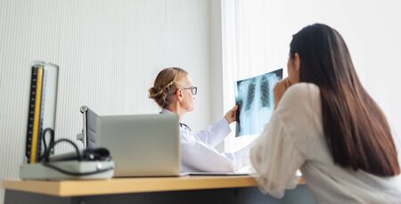 Elderly Female doctor holding and looking to young woman patient  X-ray film in medical room at hospital. Diagnosis disease about Lung. Covid-19, Coronavirus.の写真素材