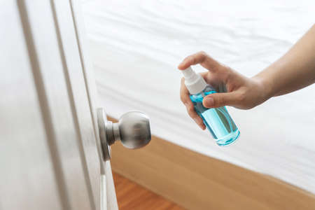 Hand applying alcohol spray to door, doorknob bedroom for protect and prevent pandemic disease,...