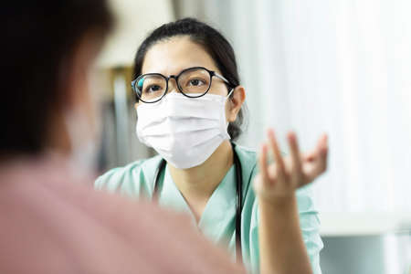 Asian woman Doctor in green uniform wear eyeglasses and surgical mask talking, consulting and giving...