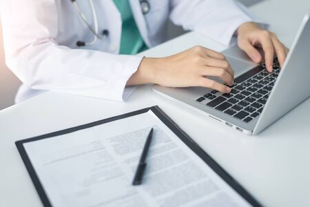 Concentrated Asian woman Doctor hands using laptop computer and working on checklist paper symptoms...