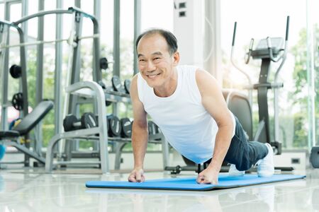 Sporty Asian Senior man in white shirt push up while exercising at the gym. Happy smiling Healthy...
