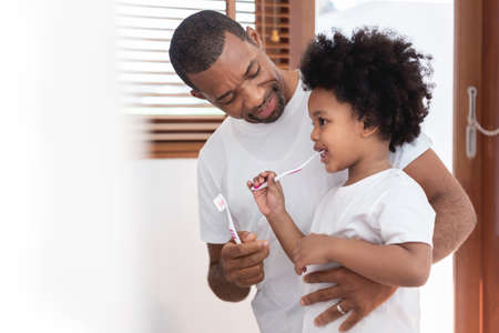 Happy African American Family, Dad teaching his son in white shirts brushing teeth in bathroom...