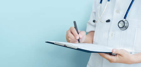 Asian female Doctor hand taking note information of patient in paperwork checklist on clipboard with  blue background, isolated, banner.の写真素材