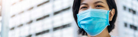 Happy Young Beautiful Asian traveler woman wearing blue protective face mask looking at camera while pandemic covid-19 or coronavirus in the city at outdoor, Confidence and Smiling face, Bannerの写真素材