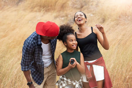 Beautiful African family having fun in autumn field outdoor, Attractive African-American man, woman and girl laughing at outside on holiday. Cheerful Father, Mother and daughter smiling togetherの写真素材