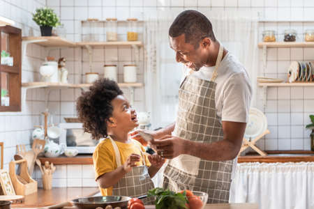 African American Father and little son playing and laughing during cooking in kitchen. Black family having fun preparing healthy food together at home. Brazilian Single dad and boy with smiling faceの写真素材