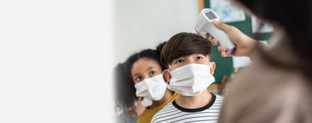 Teacher using digital thermometer for check temperature measurement on Asian boy and African...