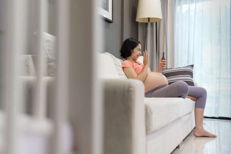 Attractive Asian Pregnant woman making video call and waving hand while talking with husband and...