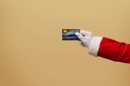 Santa Claus hand holding blue plastic credit card on golden isolated background. Shopping, Sales,...