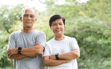 Happy Asian Senior Couple with arms crossed smiling relaxing in park.