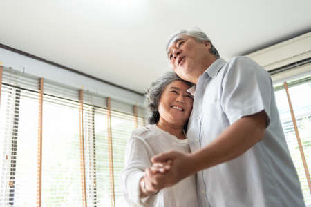 Romantic Asian Senior couple dancing at home. Happy Smiling Grandfather and Grandmother having fun Celebrating in wedding Anniversary day. Elderly man and woman holding hands together, Romance, loverの写真素材