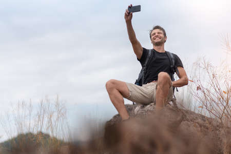 Happy man traveler with backpack taking selfie photos with smartphone in beautiful trail in...