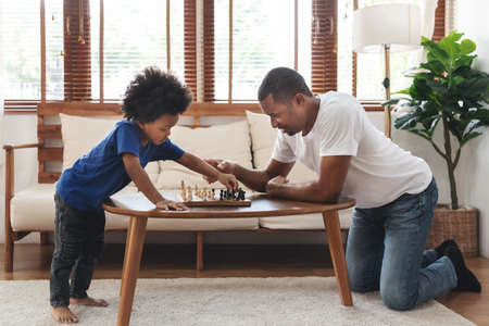 African American Father and son playing chess in living room at home together. Happy Black Family engaged in board game on holiday.の写真素材