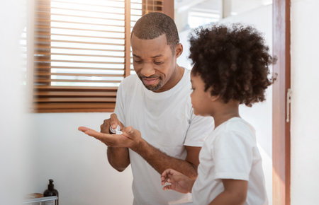 Black African American Father and little boy using shaving foam in bathroom at home together.の写真素材