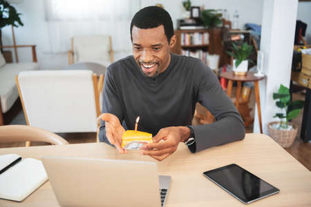 Black African American male  using laptop celebrating birthday online by video chat with birthday cake at home.の写真素材