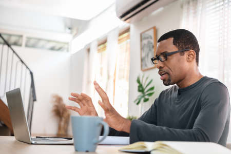 African American man having video call and working on laptop with colleague at home. Black African...