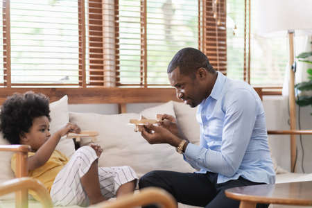 Cheerful African American Father playing airplane toys with his little son on sofa at home. Happy Black family enjoying and having fun together.の写真素材
