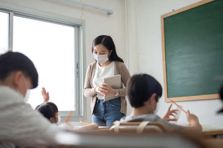 Young Asian Teacher wearing protective face mask teaching her students in classroom at the international school. Education during coronavirus pandemic.の写真素材