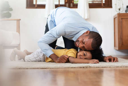 Happy African American Father playing with little child son on the floor at home together. Black family having fun on weekend.の写真素材