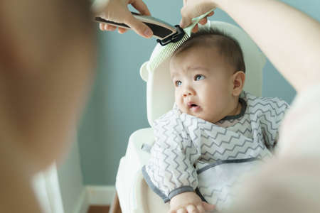 Asian little Baby boy is cutting hair by his mother with hair clipper at home.の写真素材