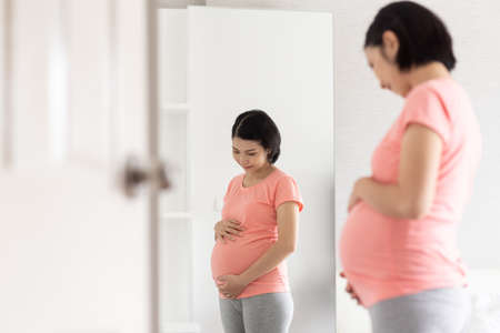 Cheerful Asian pregnant woman standing touching belly.の写真素材