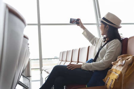 Young Asian woman traveler having online video call on smartphone while travel in vacation trip at international airport.の写真素材