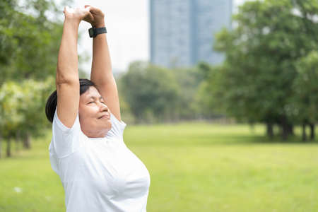 Smiling Asian senior woman stretching her arms after exercising at public park.の写真素材