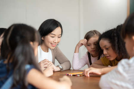 Pupils playing games with Asian female teacher together in classroom. Group of Diverse school kids having fun.の写真素材